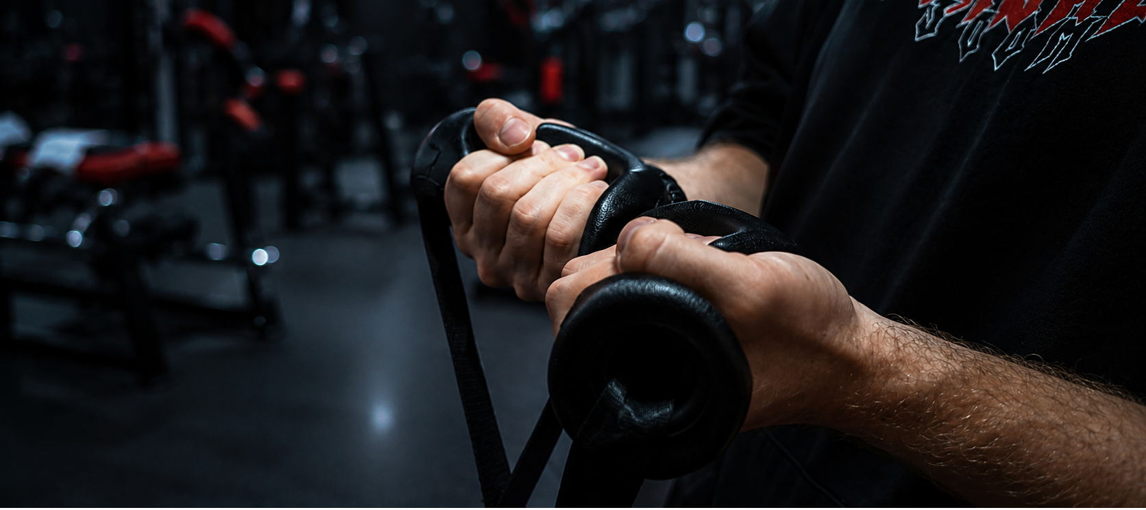 A close-up of a person's hands gripping a ergonomic attachment in a dark gym setting. 